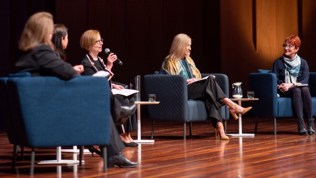 Image of 5 women seated on a stage, with julia gillard speaking into a microphone
