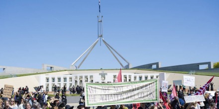 Image of march for justice protest in front of parliament house. Sign saying 'we are not satisfied! the agitation will go on'